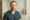 a confident male injector in scrubs poses in a clinical environment, showcasing professionalism.
